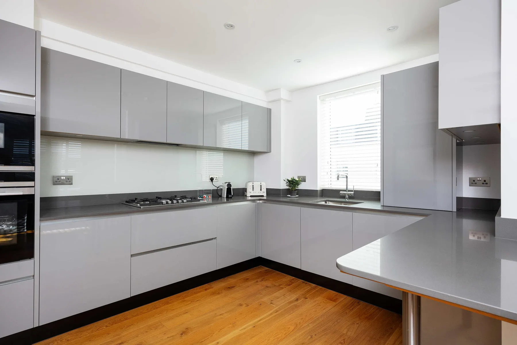 A modern kitchen with gray cabinets, dark countertops, and a wooden floor.