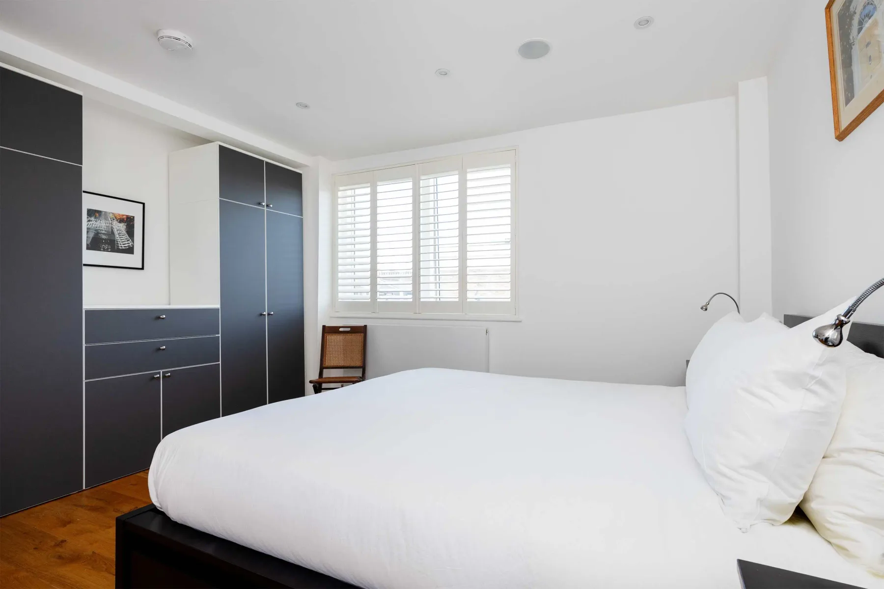 A bright bedroom with white bedding and a window with shutters.