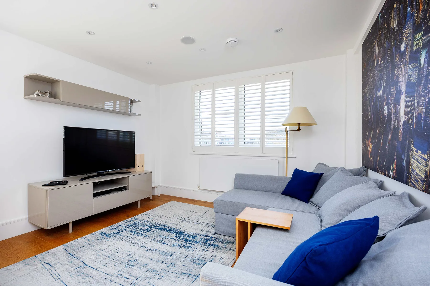 A bright living room with gray seating, a television, and large windows.