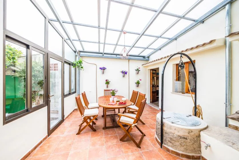 A glass-roofed patio with a dining table and a stone well.