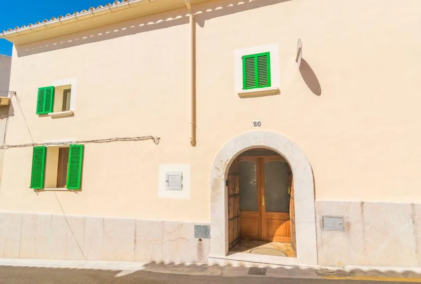 A pale stucco building facade with green shutters and an arched wooden entrance.