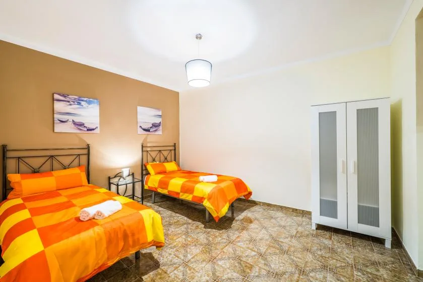 A bedroom with two orange-and-yellow beds and a white wardrobe.