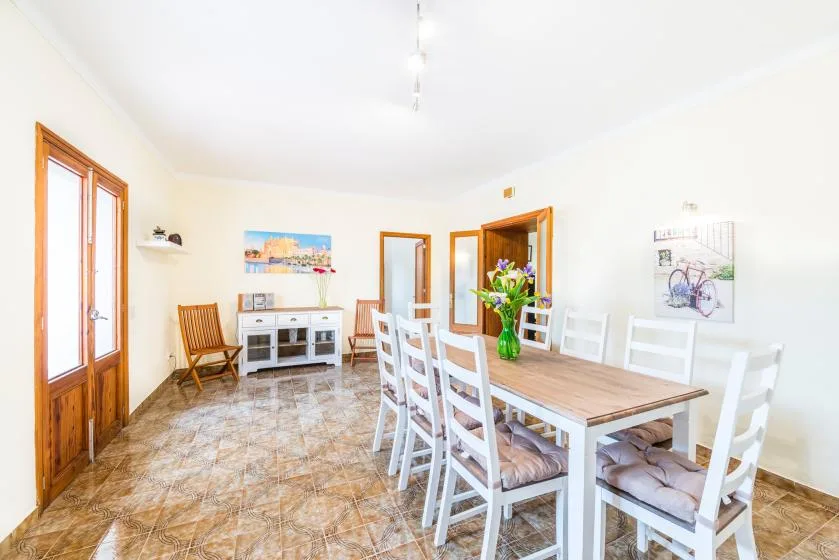 A bright dining room with a long table, white chairs, and a colorful flower arrangement.
