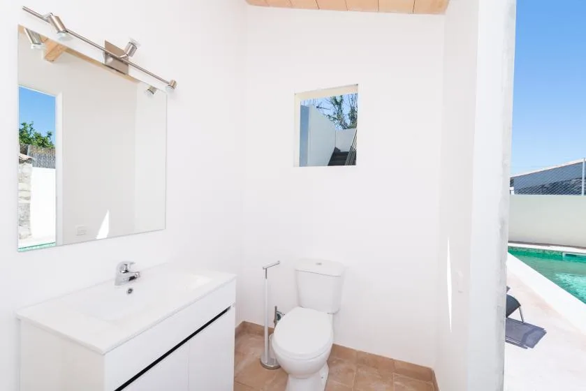 A bright bathroom with a sink, mirror, and toilet beside an outdoor pool.