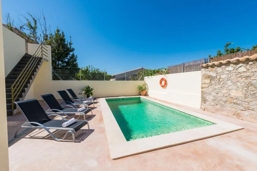 An outdoor swimming pool is surrounded by lounge seating and pale paving.