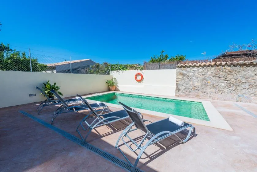 An outdoor pool area with lounge seating beside a white wall.