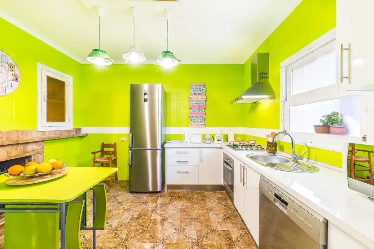 A bright kitchen with green walls, white cabinets, and a dining table.