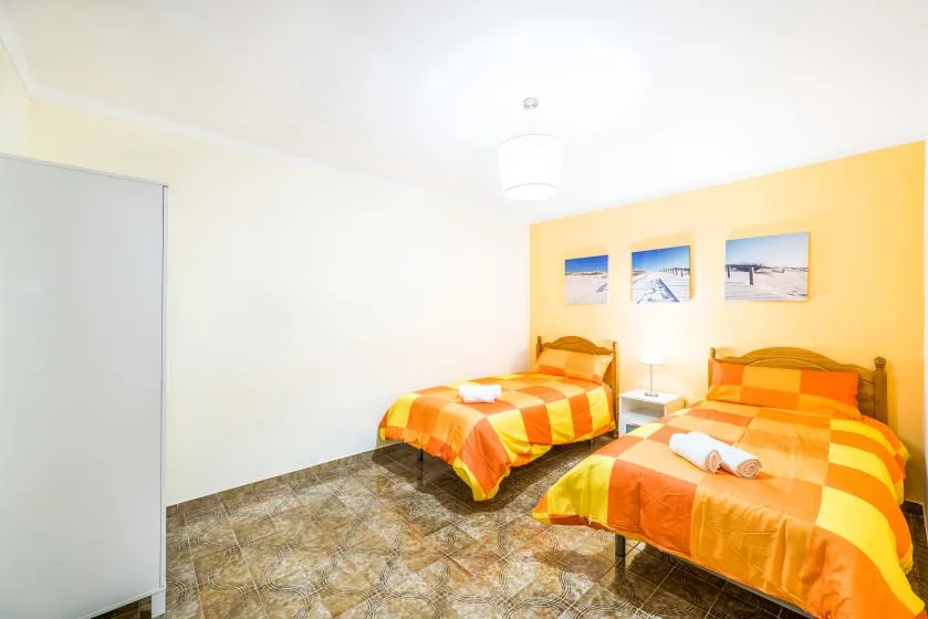 A bright bedroom with two beds dressed in orange and yellow bedding.