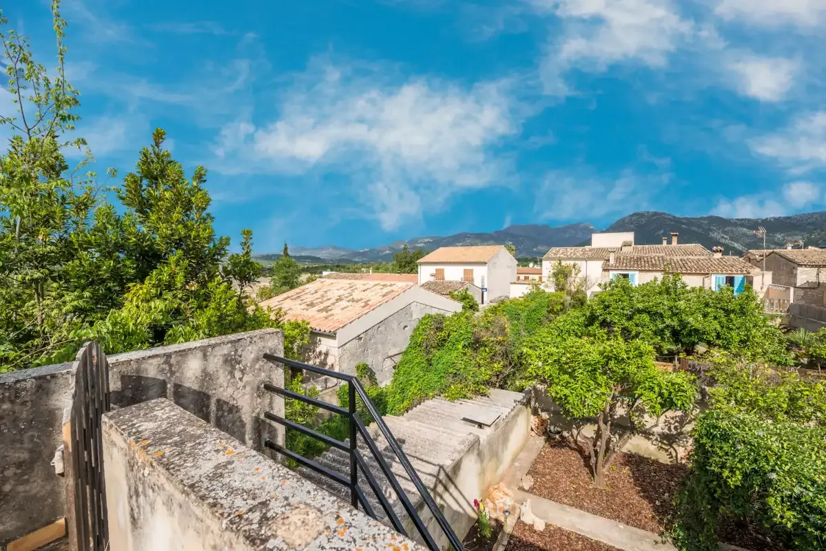 A stone terrace overlooks leafy gardens, nearby buildings, and distant hills.