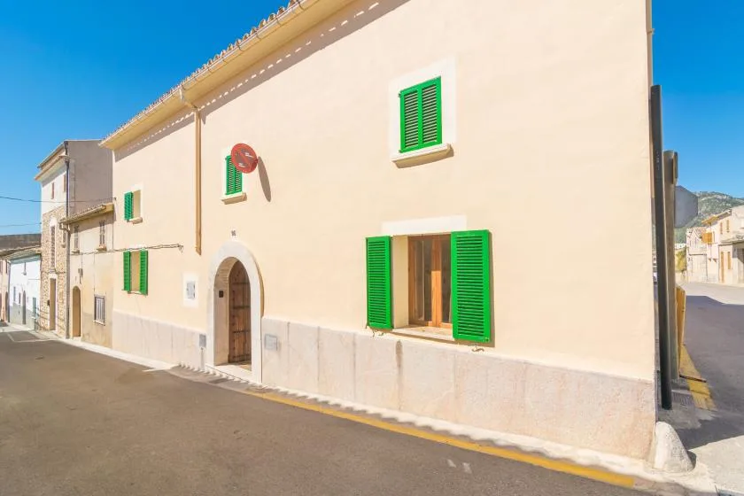 A pale building with bright green shutters stands beside a paved street.