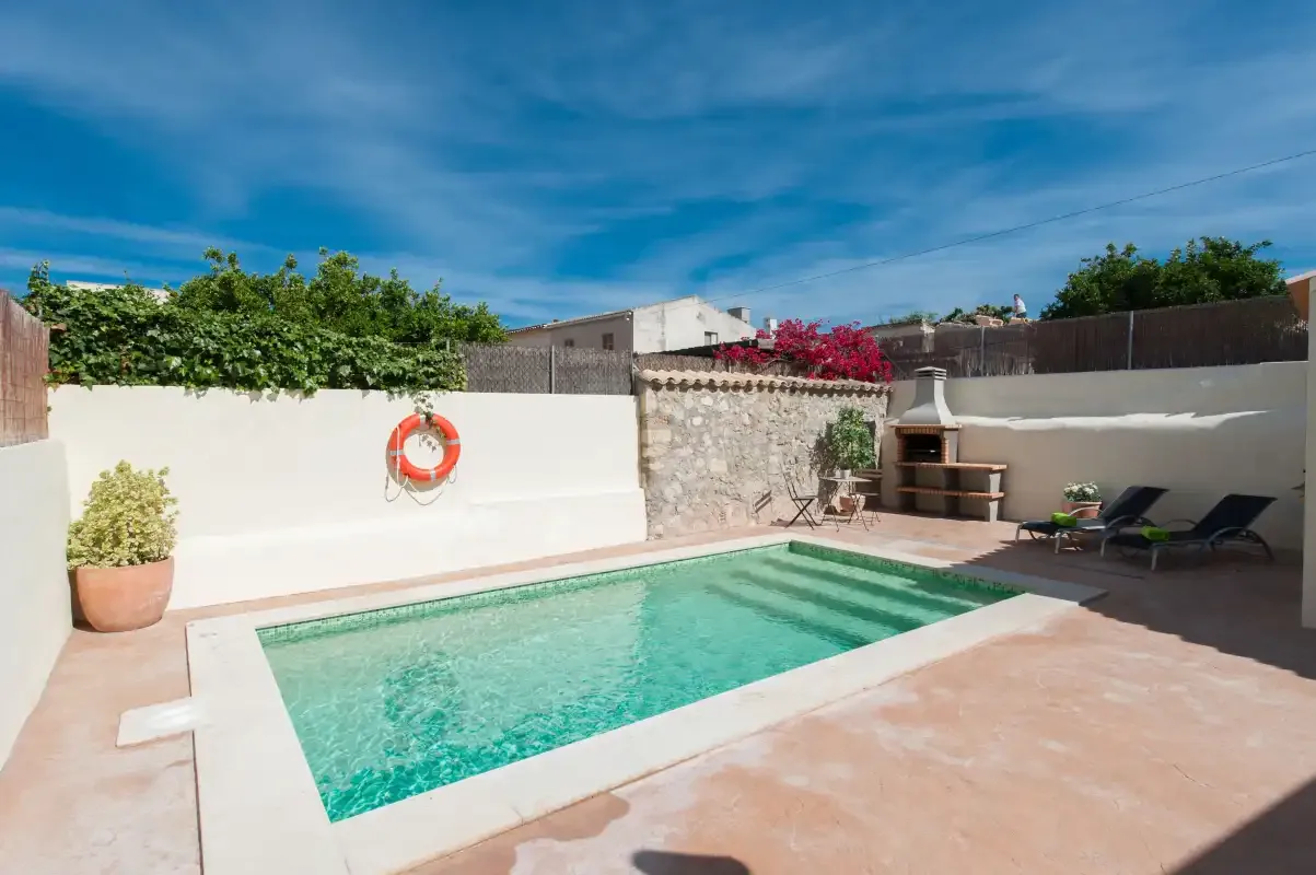 An outdoor swimming pool sits beside a patio and built-in barbecue.