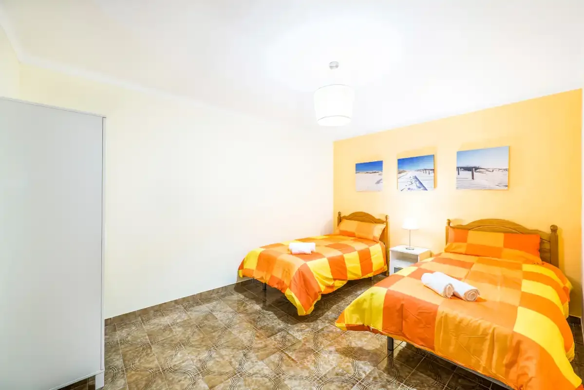 A bright bedroom with two beds dressed in orange and yellow bedding.