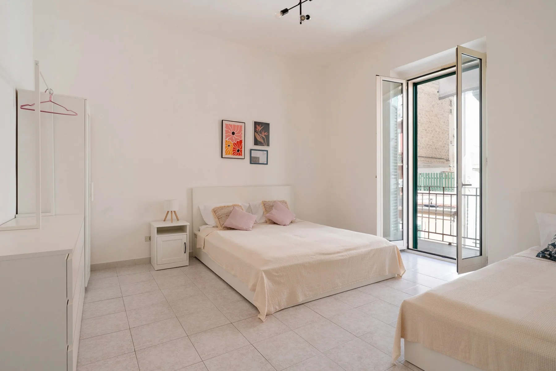 A bright bedroom with two beds and an open balcony door.
