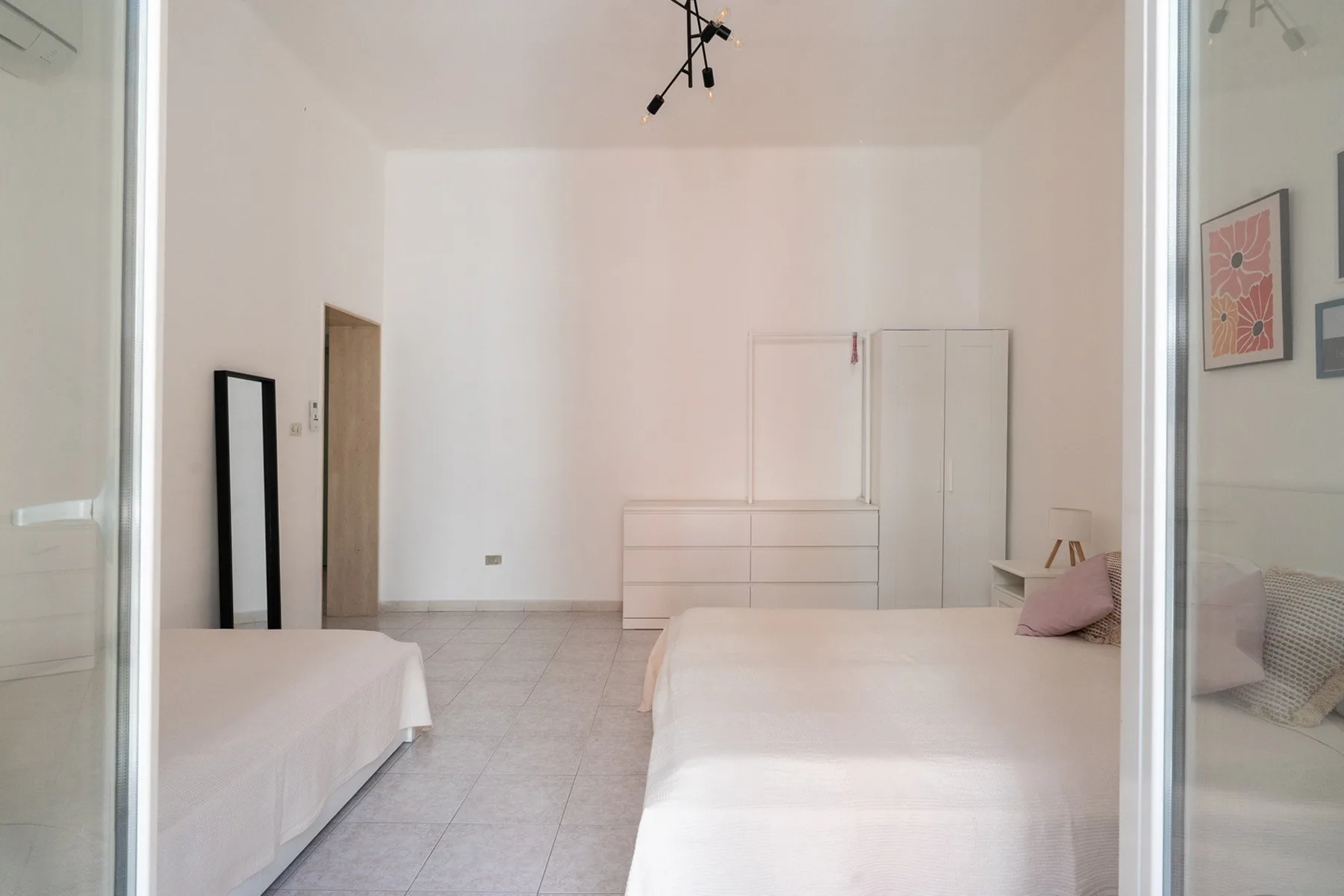 A bright bedroom with two beds and a low dresser against the far wall.