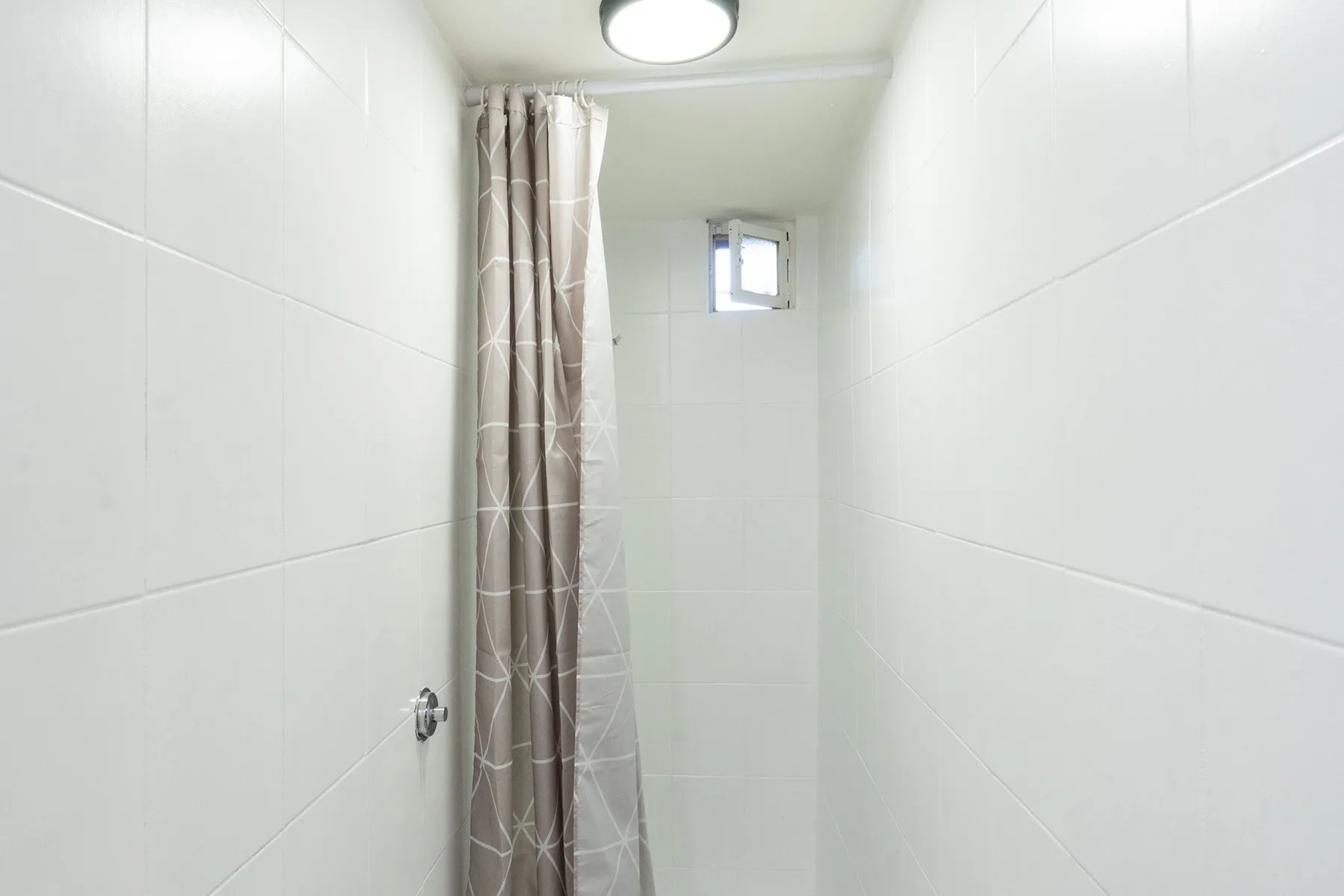 A narrow tiled shower area with a patterned curtain and small window.