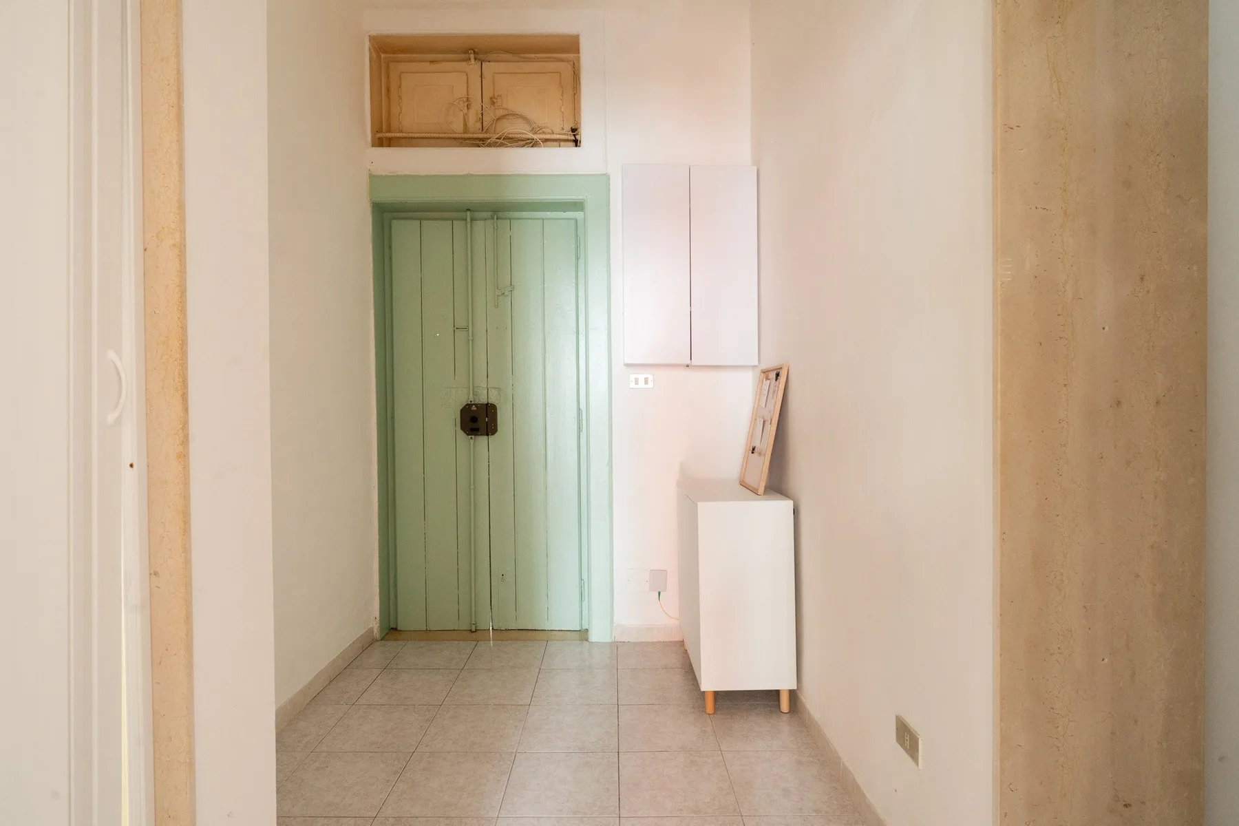 A narrow interior hallway has a green door and a small white cabinet.