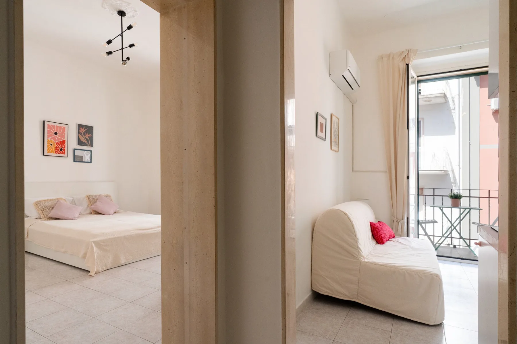 A bright bedroom with a bed and a small seating area beside a balcony.