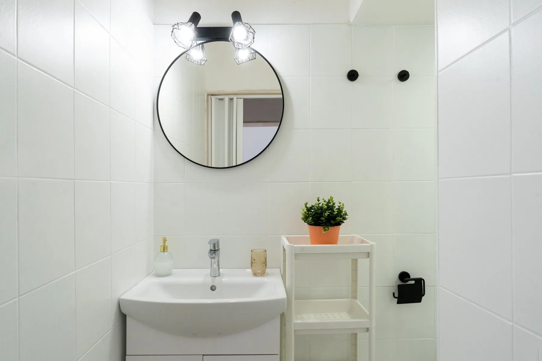 A tiled bathroom with a sink, round mirror, and a small potted plant.