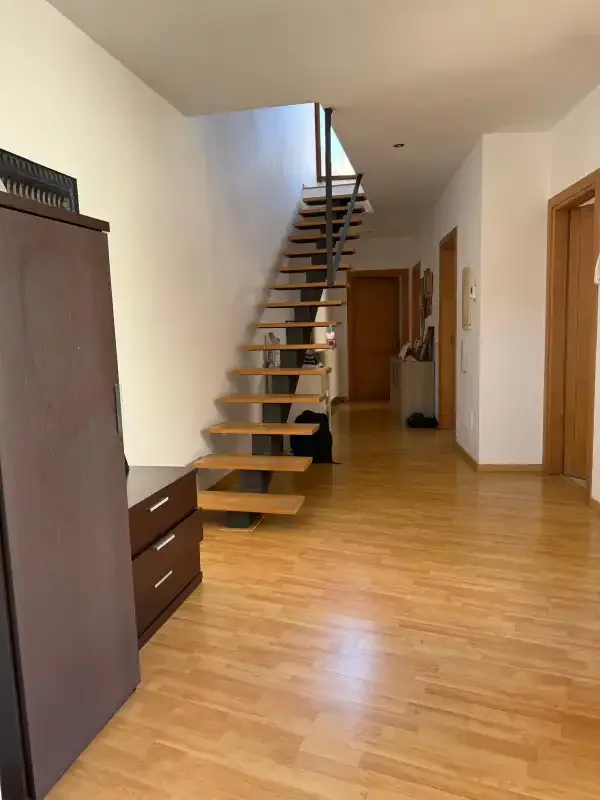 Un pasillo luminoso con una escalera flotante y suelo de madera.