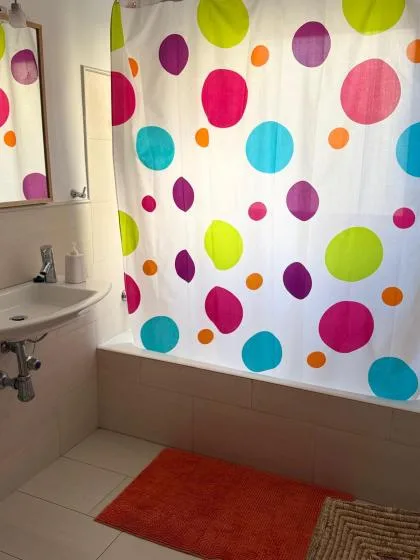 Se ven parcialmente un lavabo y una bañera junto a una cortina de ducha de lunares coloridos.