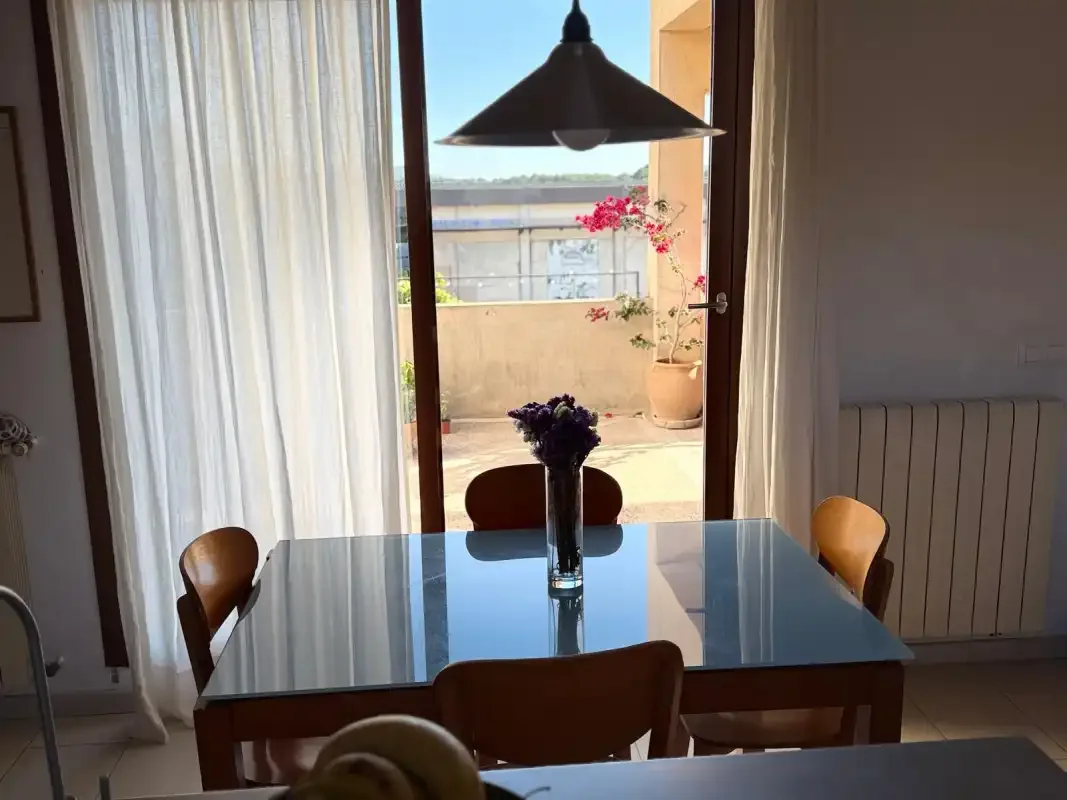 Un comedor con una mesa de cristal y una puerta abierta a un balcón.