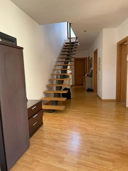 An interior hallway with an open-riser staircase and wood flooring.
