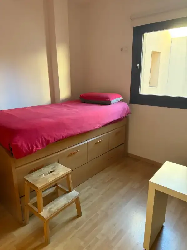Un dormitorio con una cama individual, cajones de madera y una ventana.