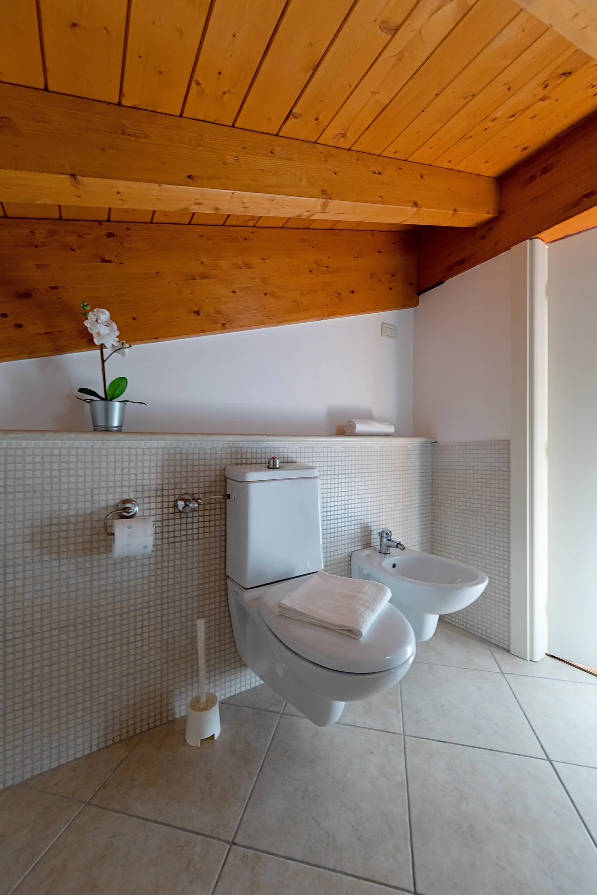 Un baño con inodoro, bidé y techo inclinado de madera.