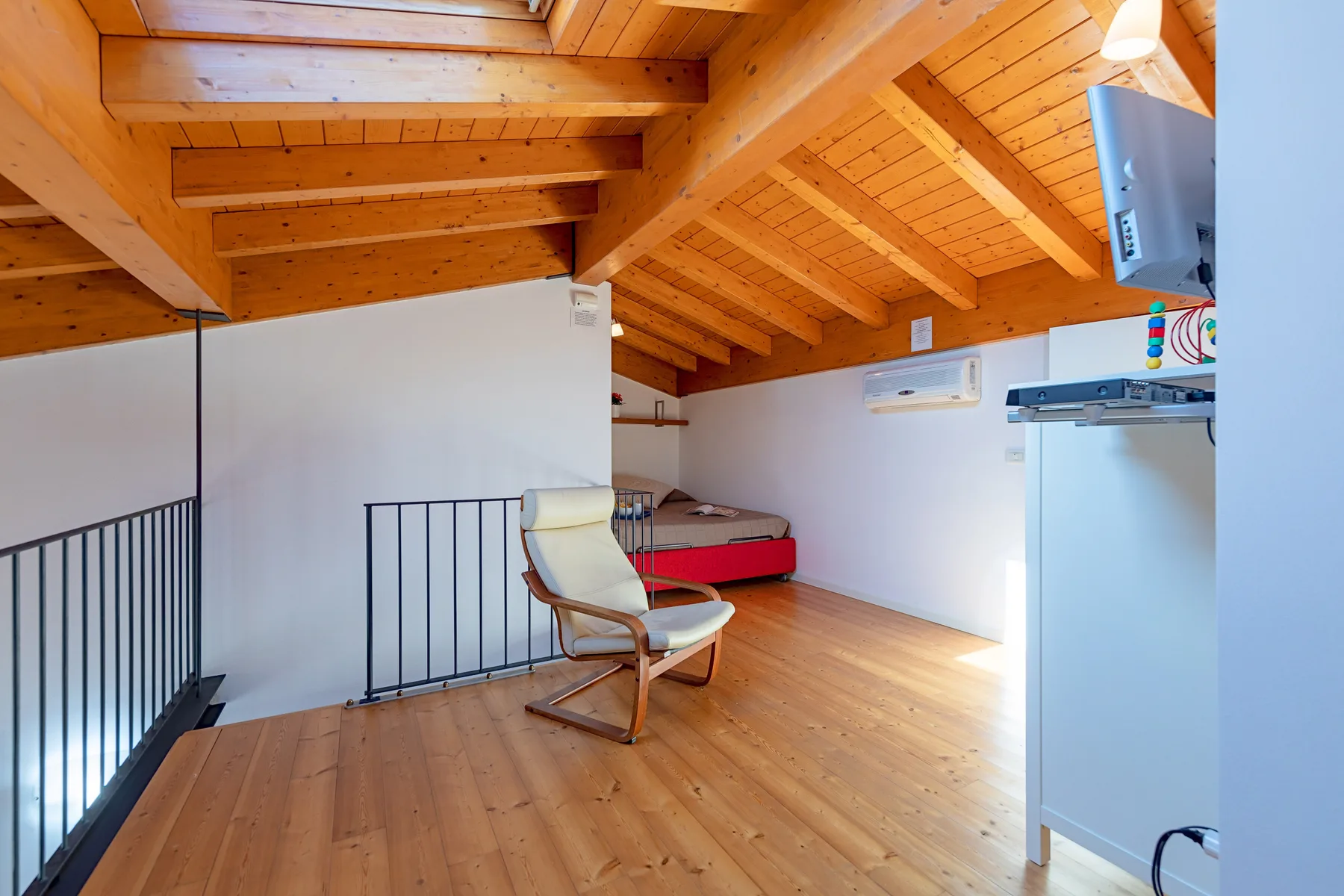 Un dormitorio tipo loft luminoso con una cama, asientos y vigas de madera a la vista.