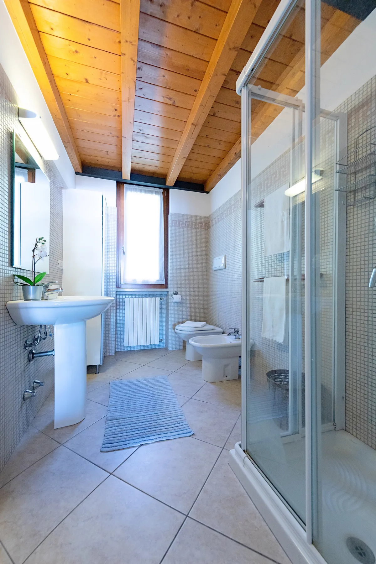 Un baño con azulejos, lavabo, inodoro y ducha con mampara de vidrio.