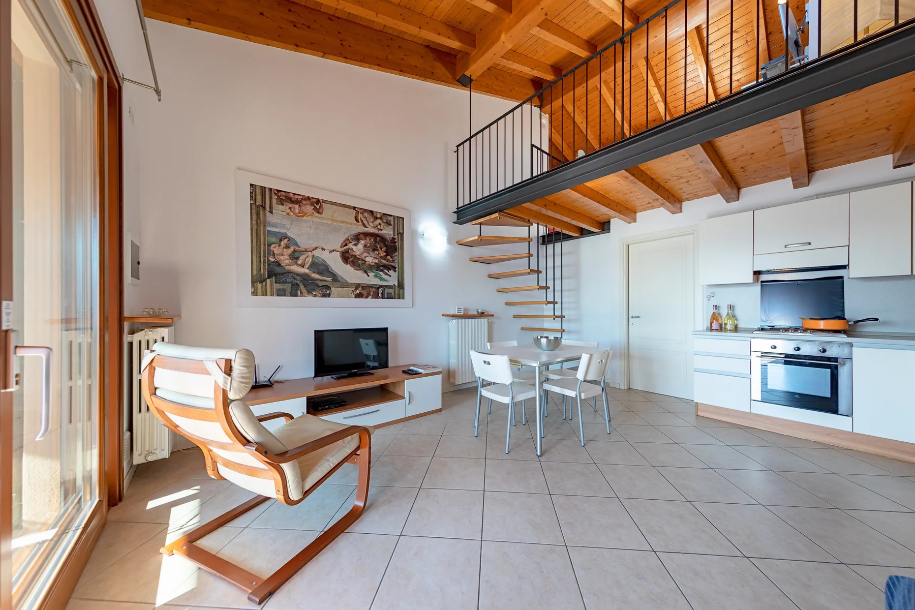 Una sala de estar de concepto abierto con mesa de comedor, cocina y escaleras al altillo.