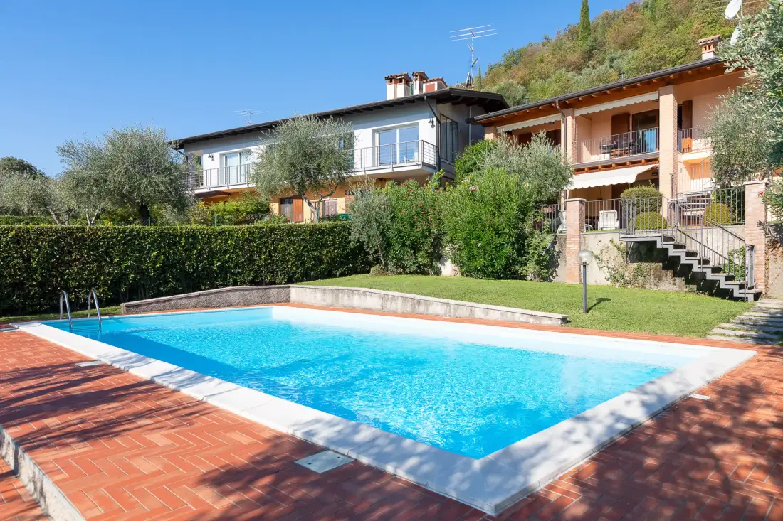 Una piscina al aire libre junto a un césped ajardinado y edificios residenciales.