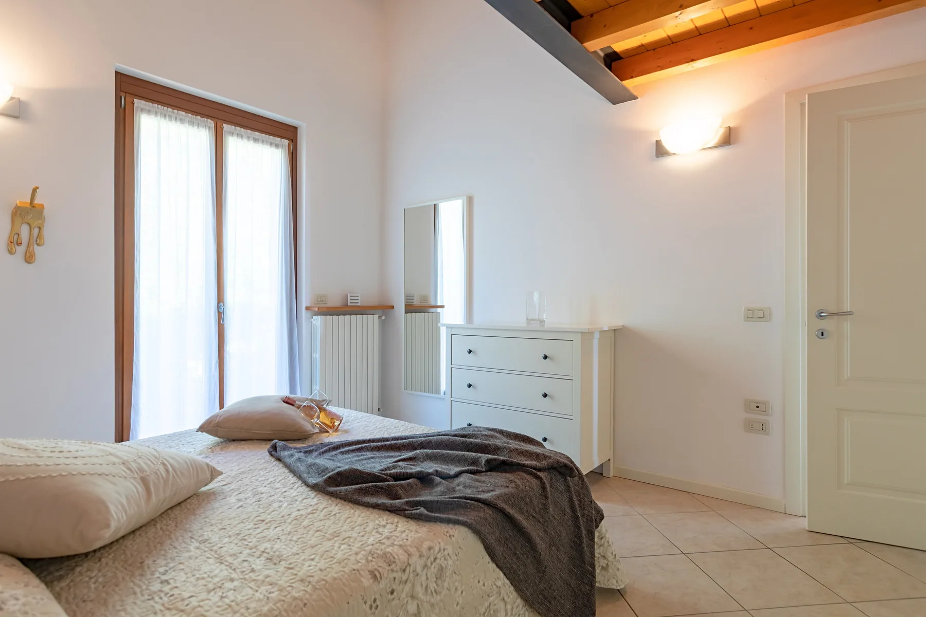 Un dormitorio con una cama, una cómoda y una puerta de vidrio que deja entrar luz natural.