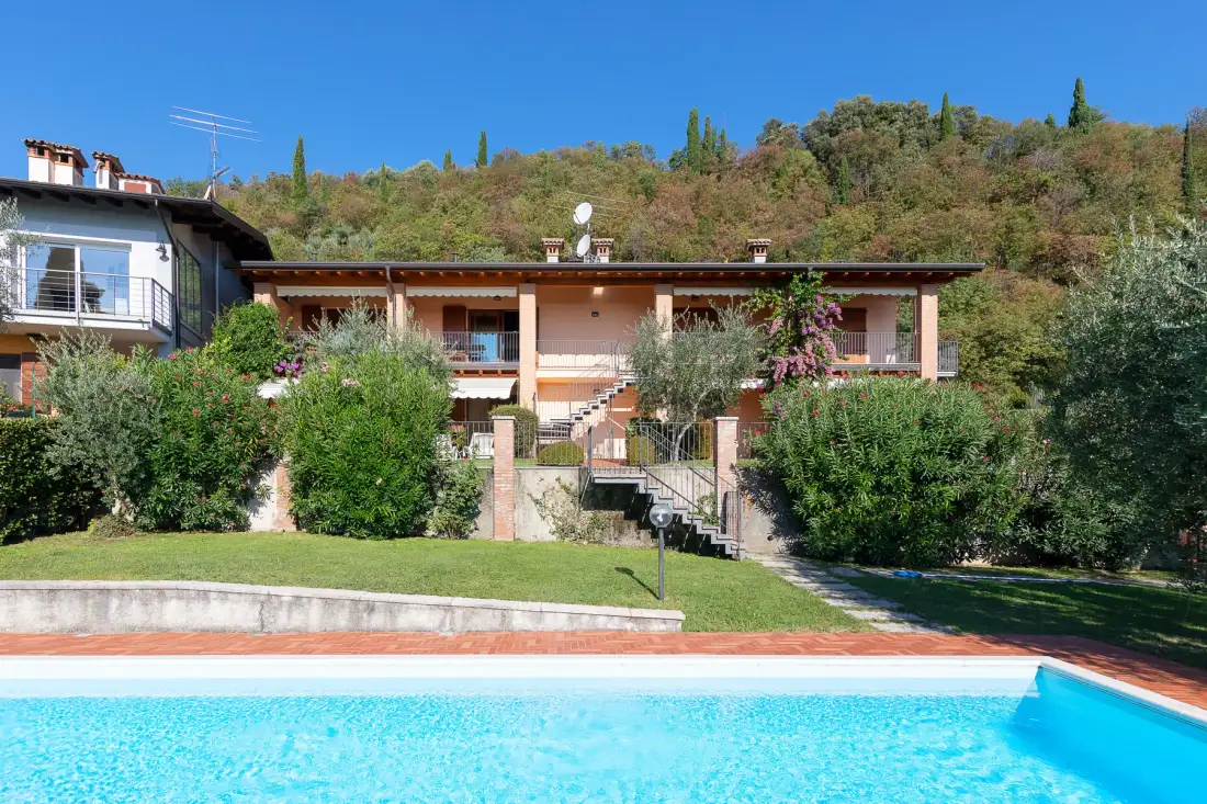 Una piscina frente a una casa baja, con colinas arboladas al fondo.