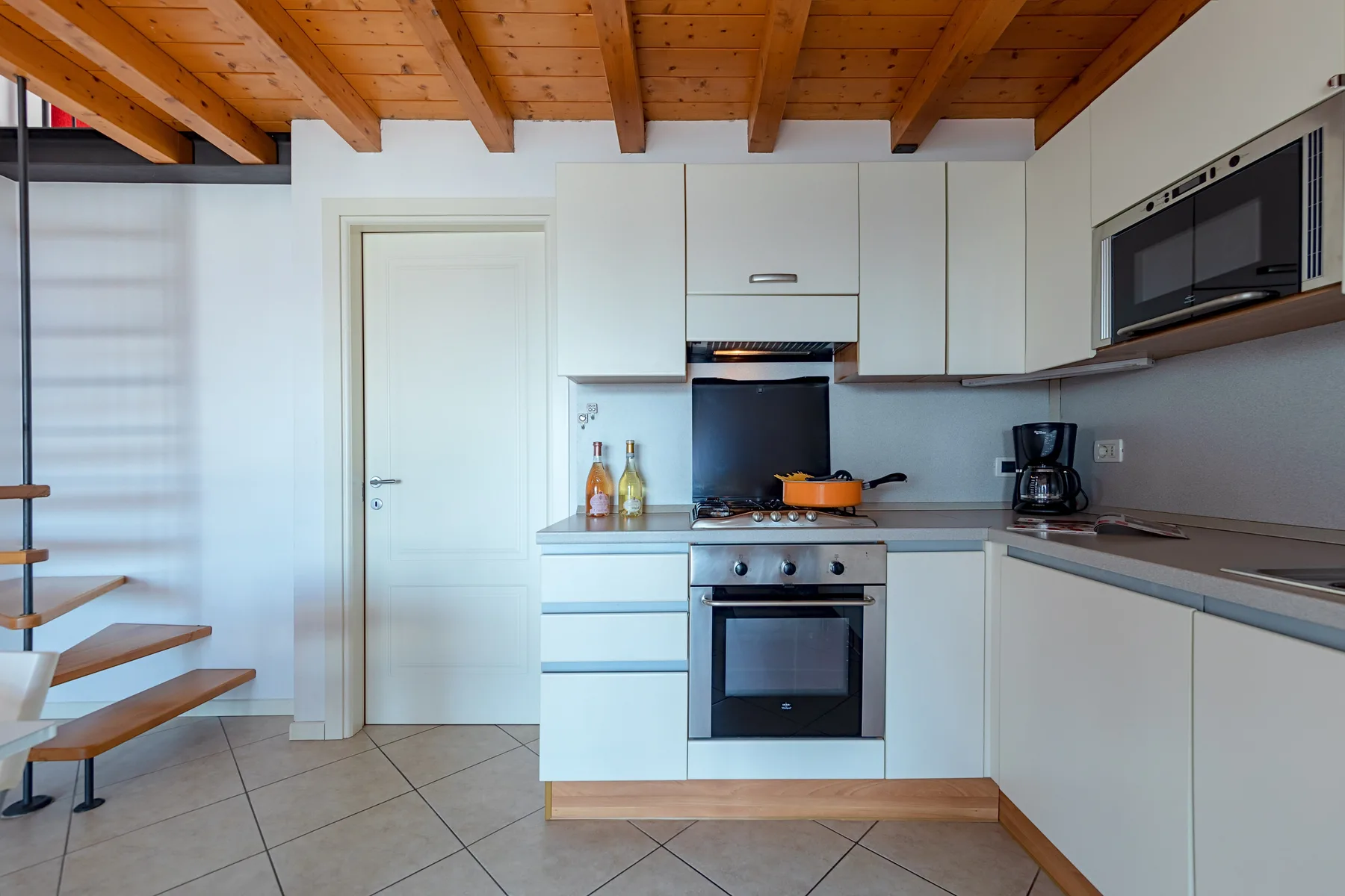 Una cocina compacta con gabinetes blancos, una estufa y un techo de madera.