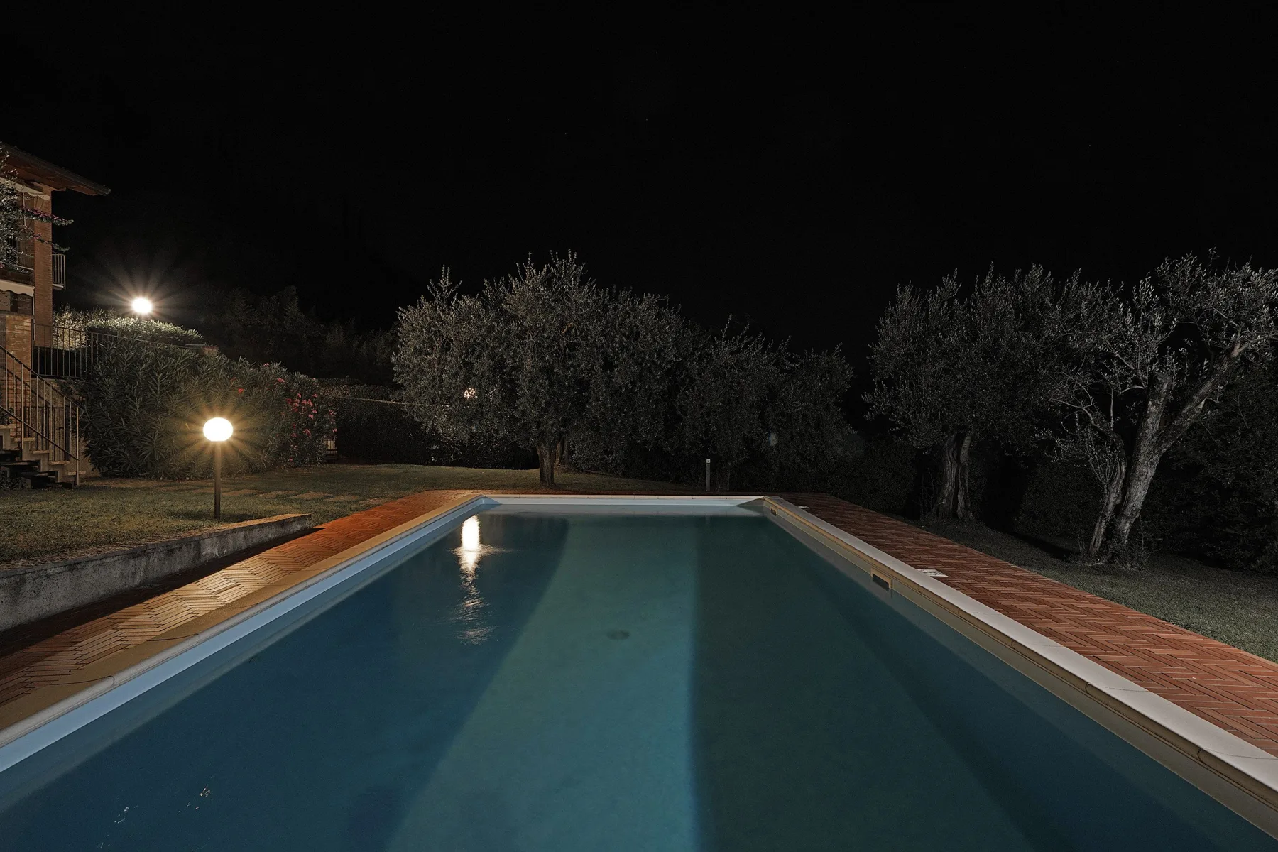 Una piscina de noche, rodeada de árboles e iluminada por luces del jardín.