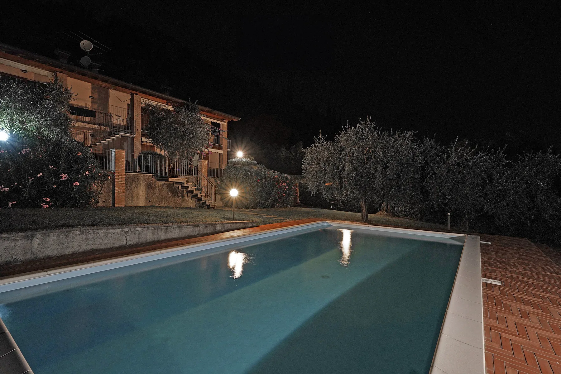 Una piscina al aire libre junto a un edificio iluminado y jardines por la noche.