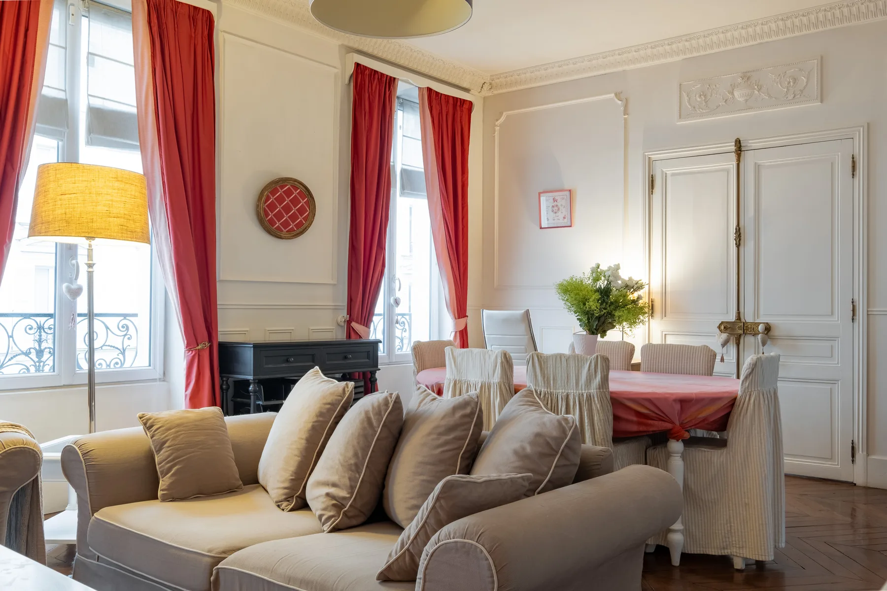 Una sala luminosa con asientos tapizados y una mesa de comedor junto a ventanas altas.