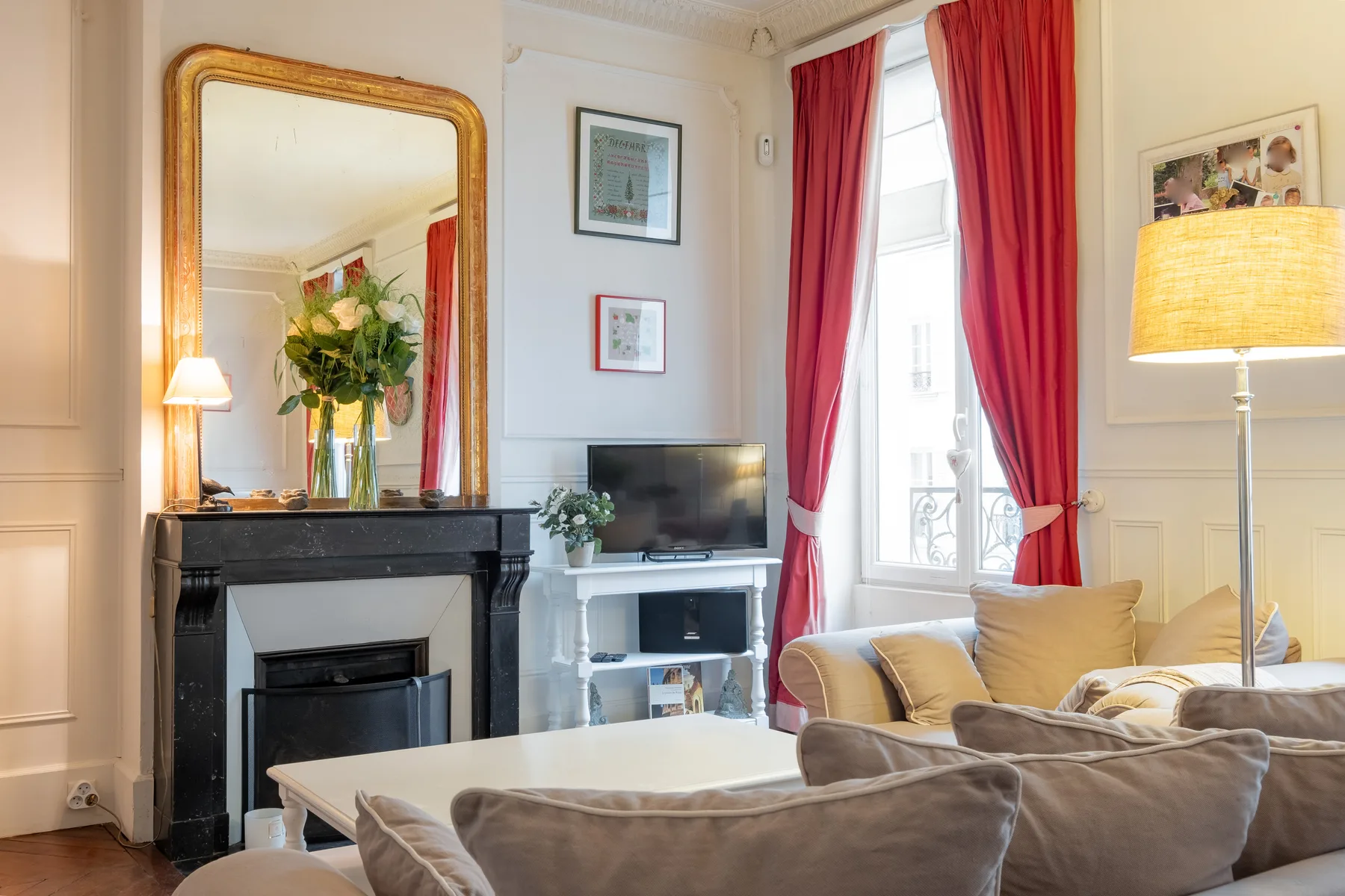 Una sala de estar con chimenea, televisor y asientos junto a una ventana alta.