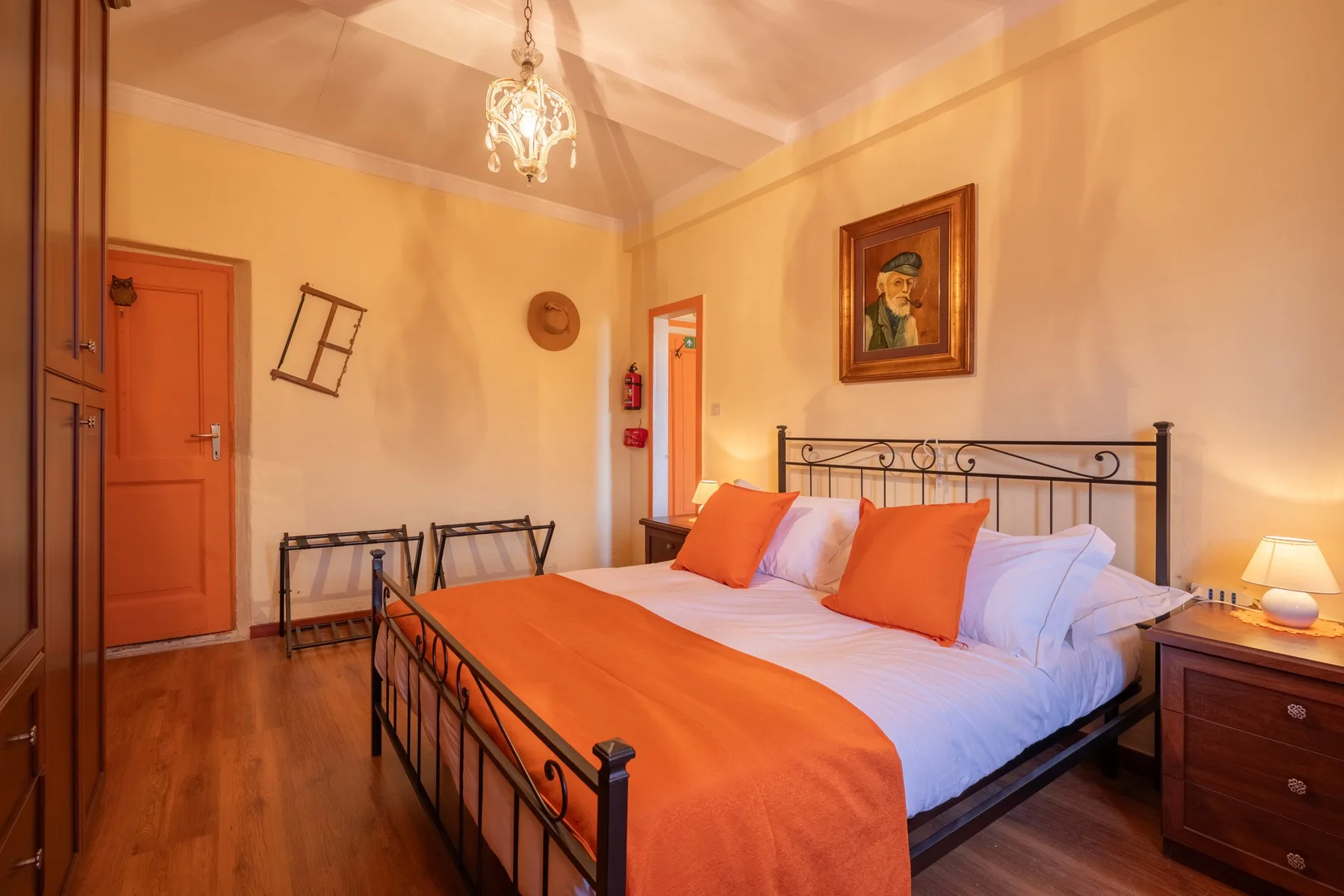 A bedroom with a metal bed, orange bedding, and warm-toned walls.