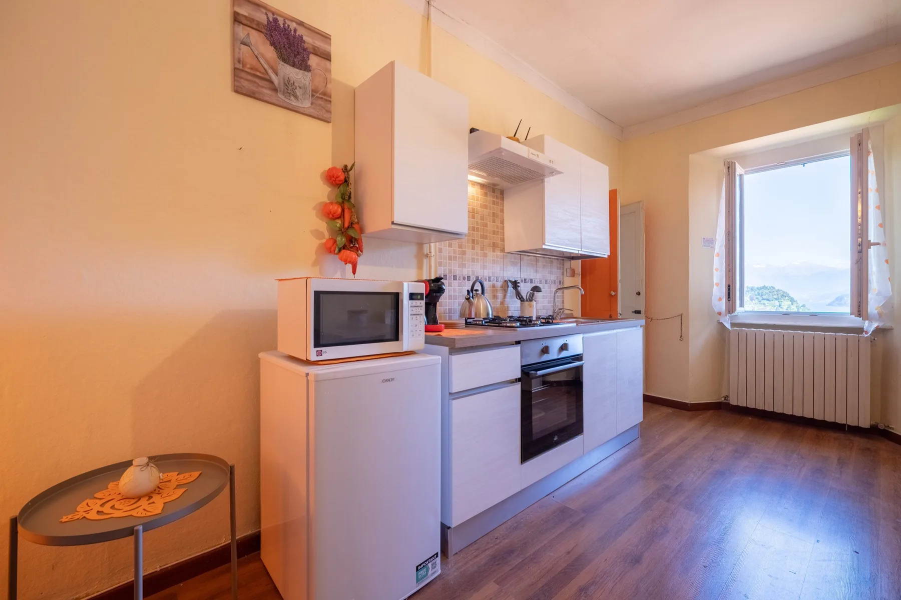 A compact kitchen with white cabinets, a refrigerator, and a window.