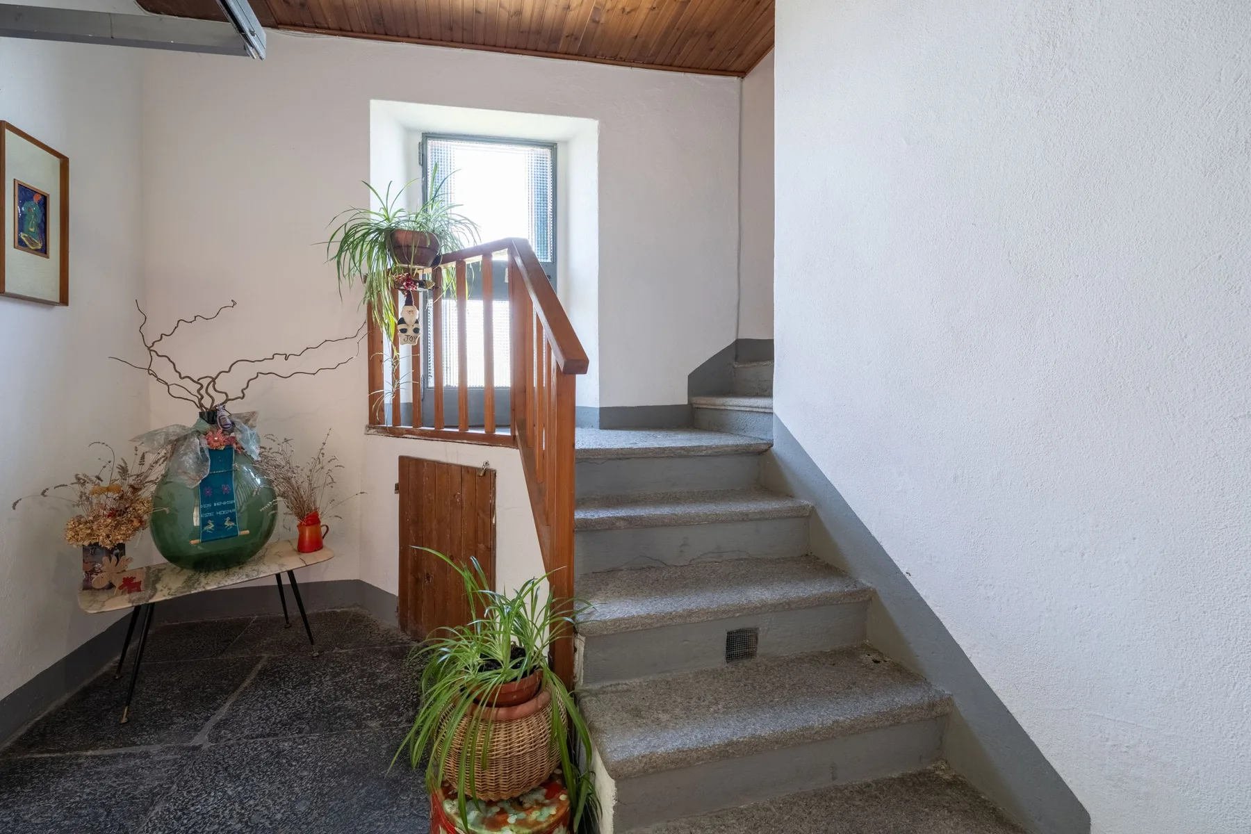 An indoor stairway with a wooden railing rises beside a small table and plants.