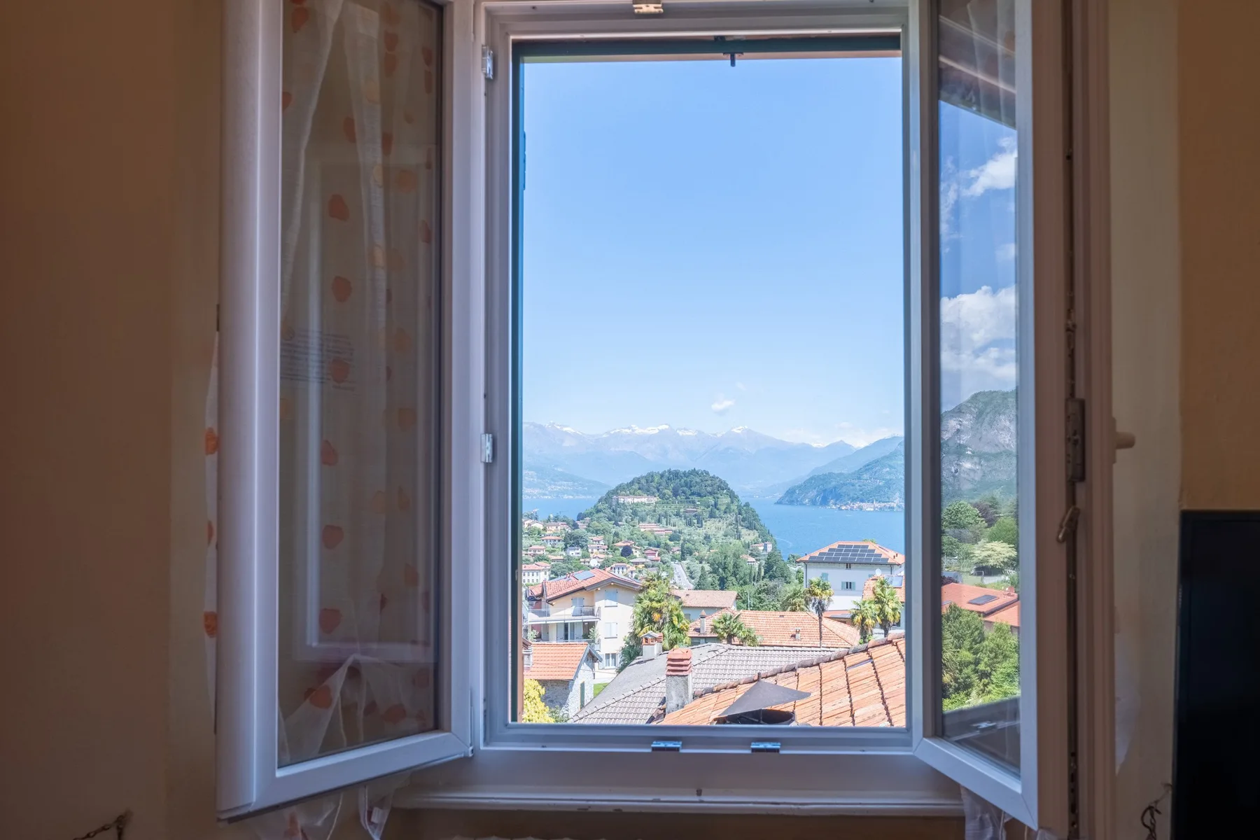 An open window overlooks a lakeside town and distant mountains.
