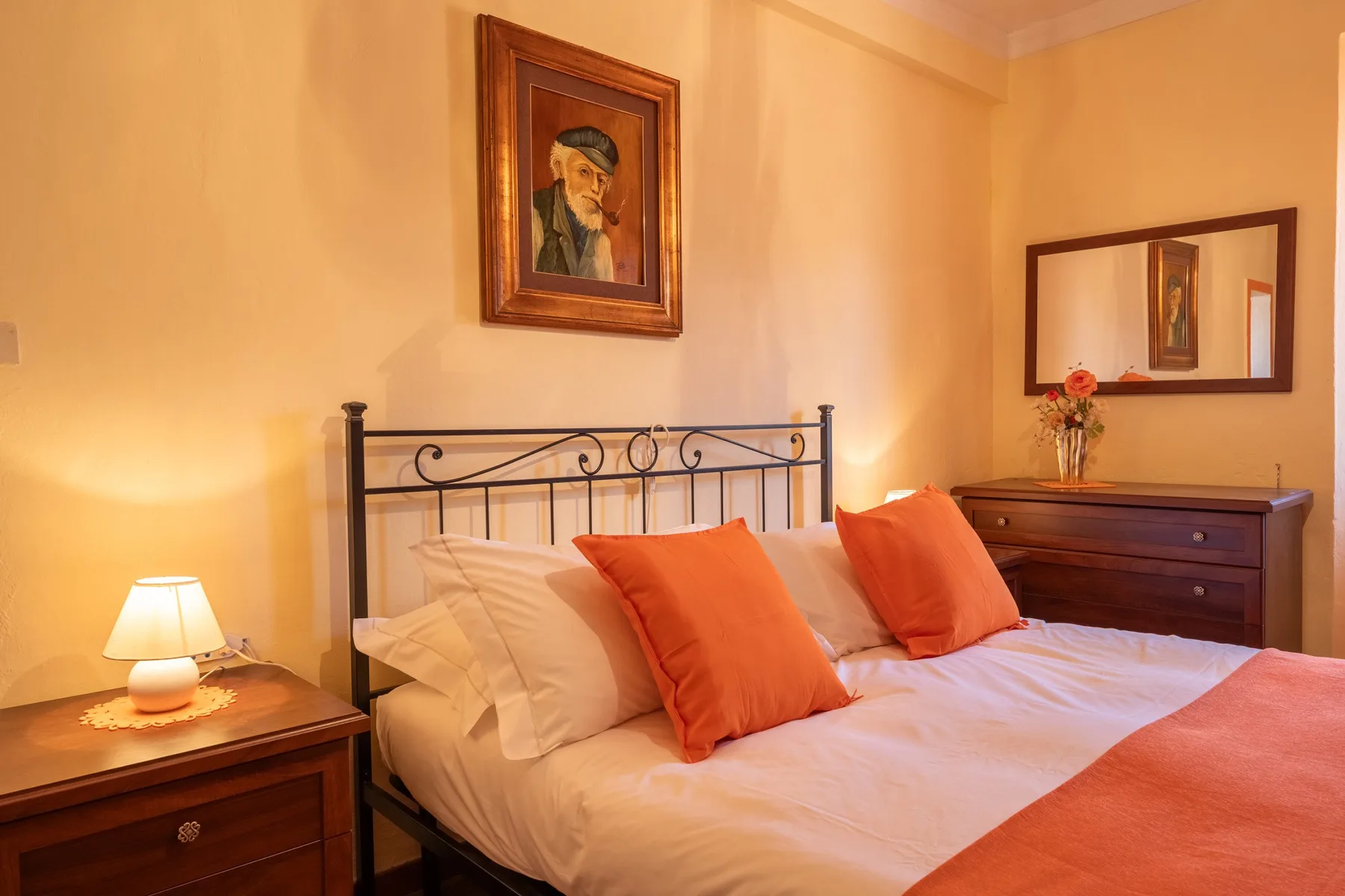 A bedroom with a metal-framed bed and warm orange accents.