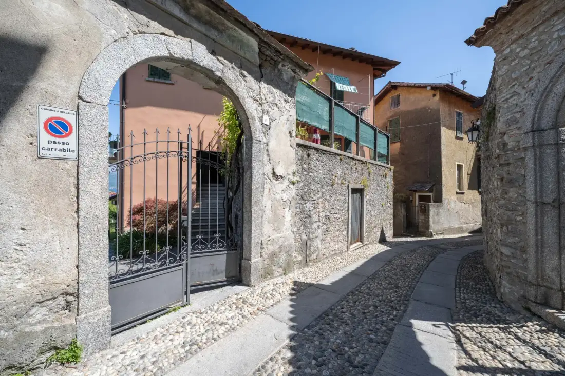 A narrow cobblestone street runs between stone buildings and an arched gate.