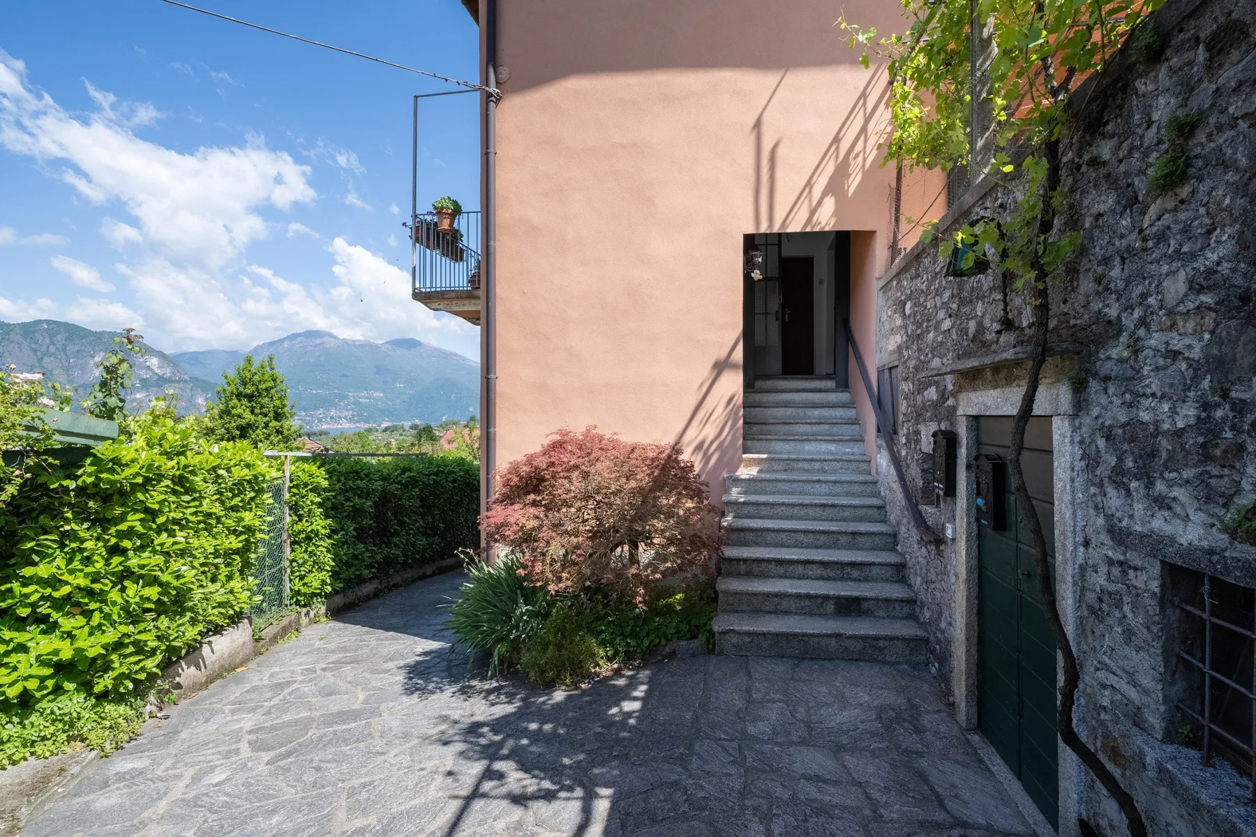 An outdoor stone-paved walkway leads to stairs beside a pink building and stone wall.
