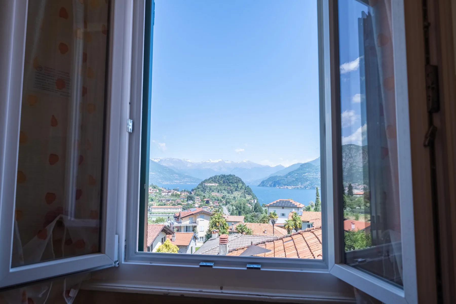 A view of a lake and surrounding mountains through an open window.