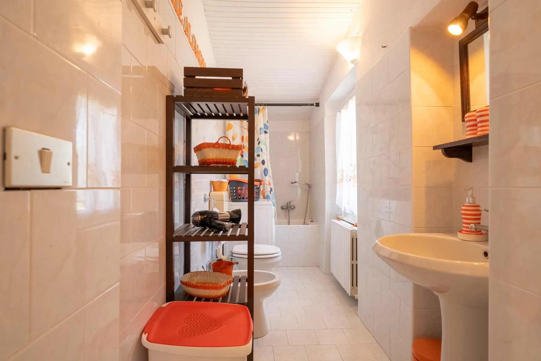 A tiled bathroom with a sink, toilet, and shelving.