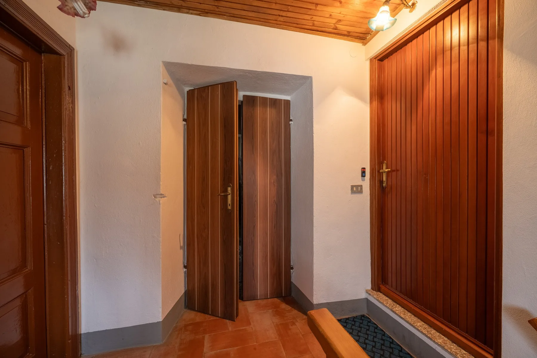 An interior entryway with wooden doors and terracotta-colored floor tiles.