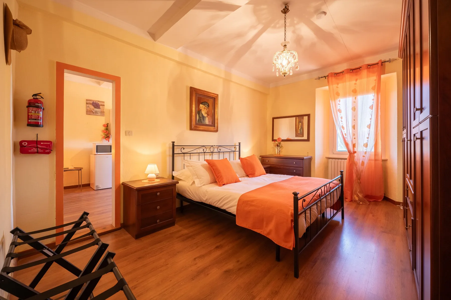 A bedroom with a metal bed, orange bedding, and a sunlit window.